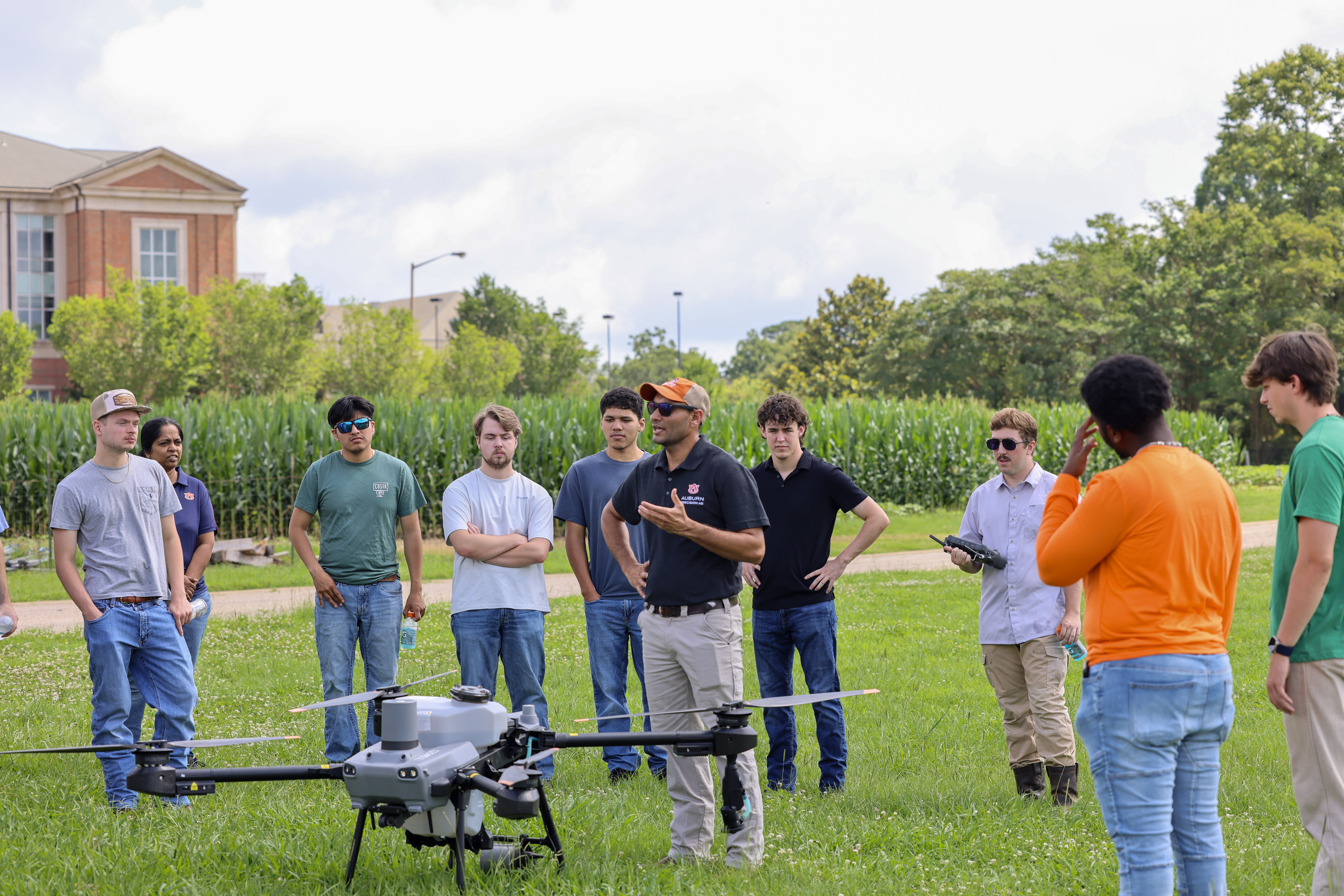 Auburn agriculture instructor lecturing a group of students in front of an agricultural drone, outdoors.