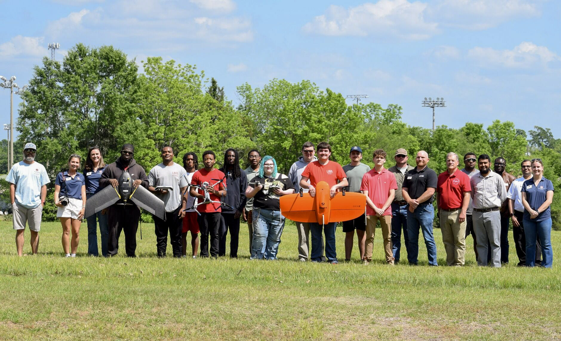 Group of students standing in a line, with two students holding onto agricultural drones.